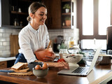 Young woman cooking in the kitchen. Beautiful woman following recipe on laptop and preparing delicious food.