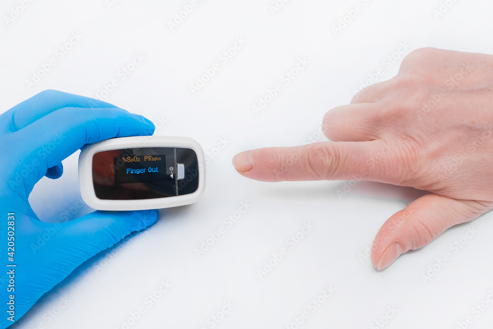 The doctor's hand in a latex medical glove holds a device to measure oxygen in the blood, pulsexymeter with the finger of an elderly woman on a white background The doctor's hand in a latex medical glove holds a device to measure oxygen in the blood, pulsexymeter with the finger of an elderly woman on a white background