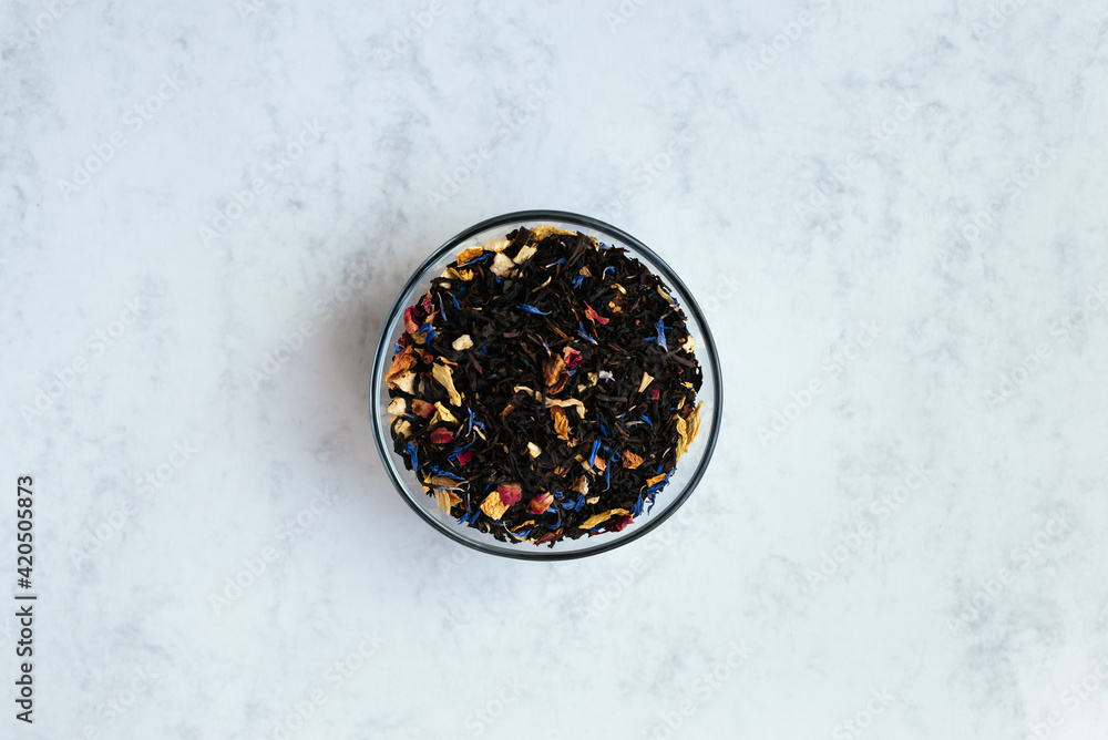Bowl full of black tea mixed with flower petals on a marble background Bowl full of black tea mixed with flower petals on a marble background