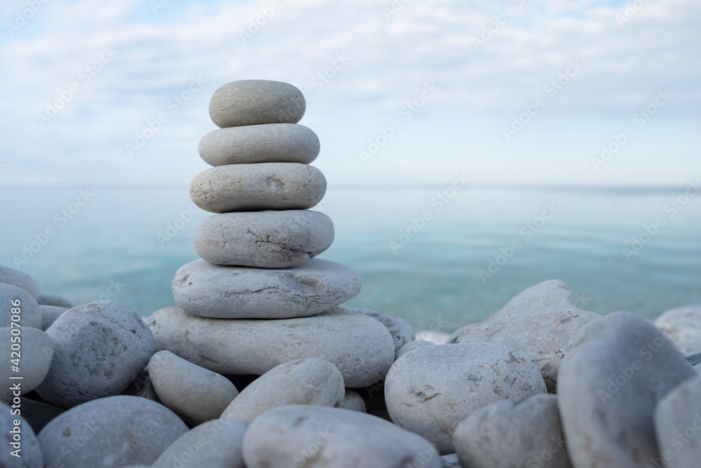 Flat rocks stacked on top of each other standing vertically on the beach, blue water and sky out of focus in the background, soft light. Balance, harmony, relaxation and peace concept. Space for copy. Flat rocks stacked on top of each other standing vertically on the beach, blue water and sky out of focus in the background, soft light. Balance, harmony, relaxation and peace concept. Space for copy.