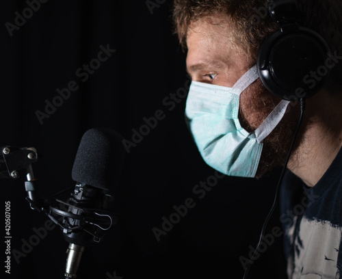 Masked man talking to a condenser microphone in isolated studio portrait shot