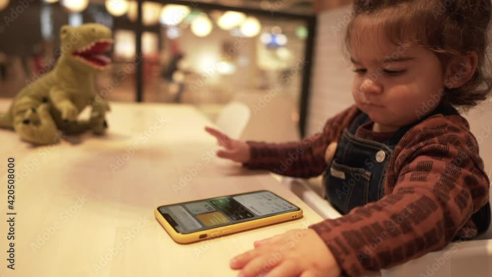 Cute Toddler Boy Sitting On High Chair In A Restaurant, Playing With Smartphone - close up Cute Toddler Boy Sitting On High Chair In A Restaurant, Playing With Smartphone - close up