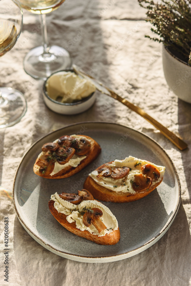 Bruschettas or toasts with cheese and fried mushrooms with thyme served with glasses of wine on greige linen tablecloth