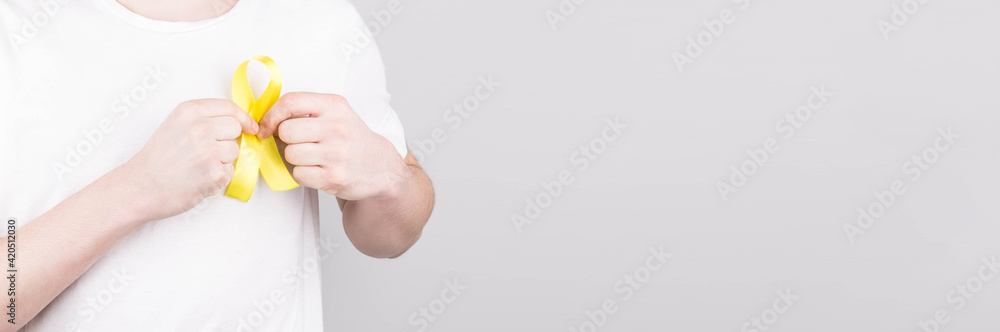 Young man in white t-shirt holding yellow ribbon awareness symbol for suicide, sarcoma bone cancer, bladder cancer, liver cancer and childhood cancer concept. Health care. Copyspace. Young man in white t-shirt holding yellow ribbon awareness symbol for suicide, sarcoma bone cancer, bladder cancer, liver cancer and childhood cancer concept. Health care. Copyspace.