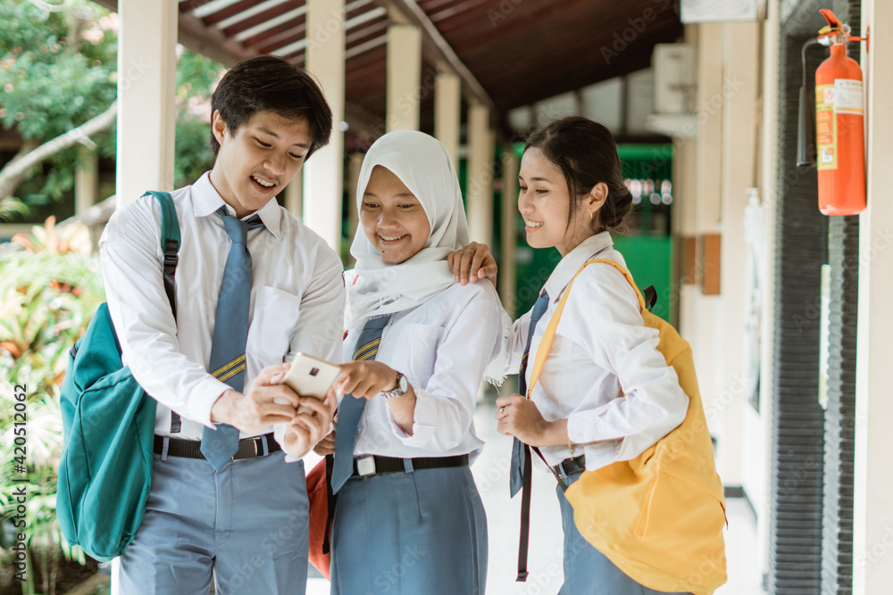 a boy and friends high school students look together with point to the mobile phone screen while chatting together at school corridor