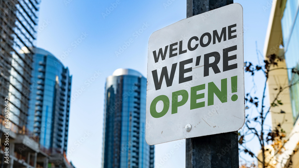 Welcome We're Open Worn Sign in Downtown city setting