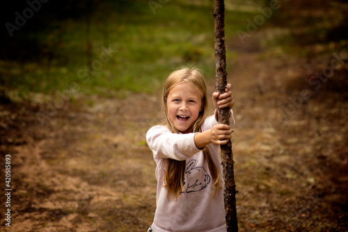 a 10-year-old girl with blonde hair climbed a tree in the forest, selective focus