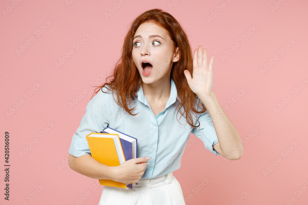 Young curious nosy redhead student woman in blue shirt hold book try to hear you overhear listening intently isolated on pastel pink background studio Education high school university college concept Young curious nosy redhead student woman in blue shirt hold book try to hear you overhear listening intently isolated on pastel pink background studio Education high school university college concept
