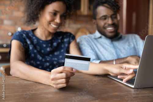 Pay money safe. Blurred shot of millennial afro american spouses sit by laptop at cozy home office make cashless payment at web store check digital wallet. Focus on wife hand holding credit bank card