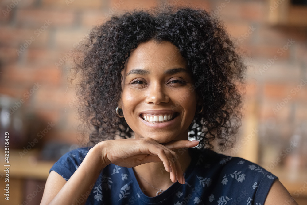 Fototapeta premium Headshot portrait of happy joyful young african american female show beautiful teeth in white cheerful smile. Adorable laughing millennial black woman looking at camera flirtatiously touching chin