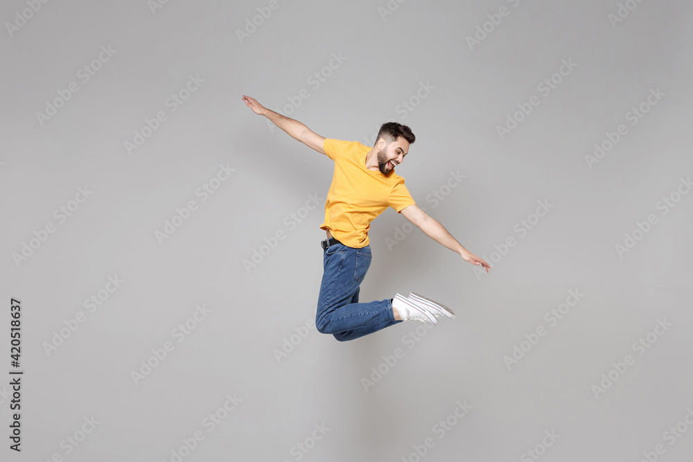 Full length of young bearded student smiling happy cheerful overjoyed man 20s in yellow basic t-shirt jump high looking aside flying outstretched hands isolated on grey background studio portrait