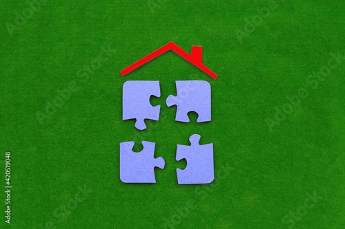 The roof of the house is red, four puzzles are blue on a green background. The concept of shared ownership, the real estate market.