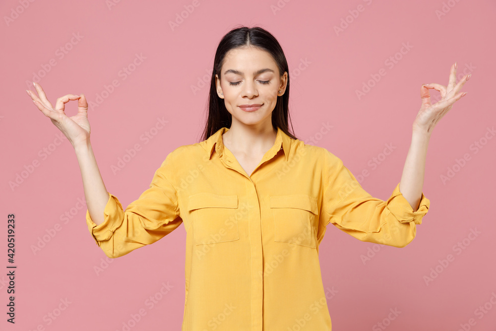 Young pensive brunette positive cute latin woman 20s wear yellow casual shirt hold hands in yoga gesture, relaxing meditating, trying to calm down isolated on pastel pink background studio portrait Young pensive brunette positive cute latin woman 20s wear yellow casual shirt hold hands in yoga gesture, relaxing meditating, trying to calm down isolated on pastel pink background studio portrait