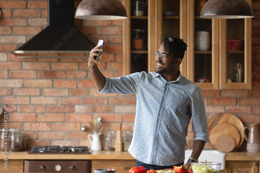 My culinary feats. Overjoyed afro caribbean male hipster shoot selfie on phone at home kitchen to share at social networks. Joyful young black male posing for self picture at moment of cooking food - obrazy, fototapety, plakaty 