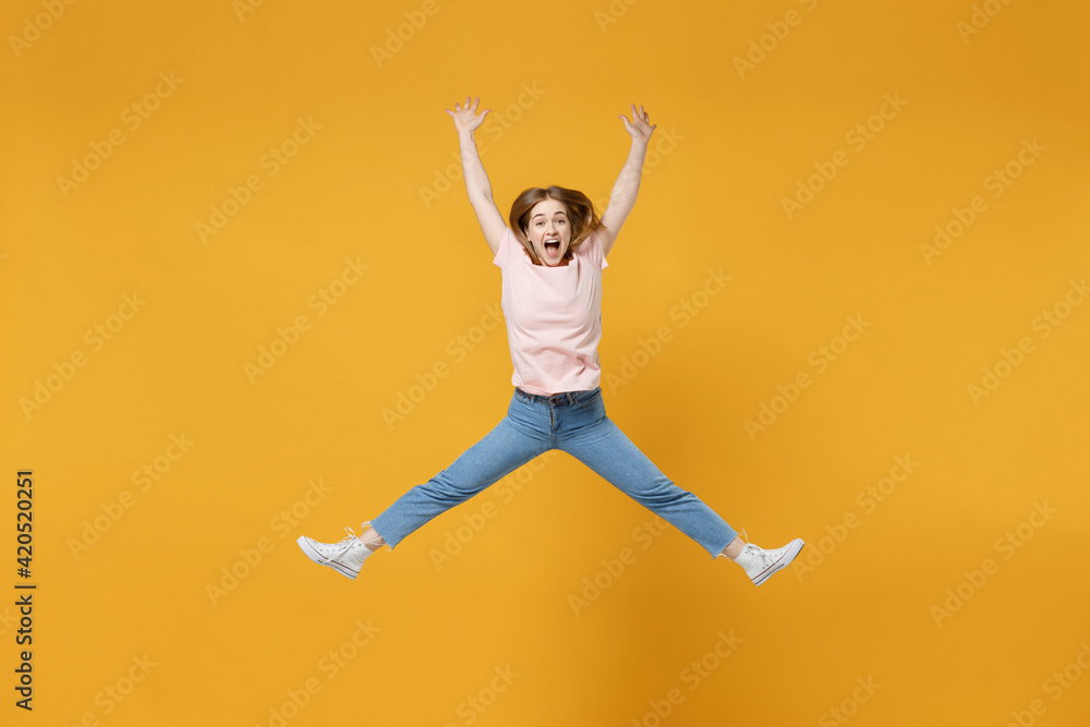 Full length of young overjoyed energetic excited woman wearing basic pastel pink t-shirt jumping high with outstretched hands, legs look camera scream isolated on yellow background studio portrait