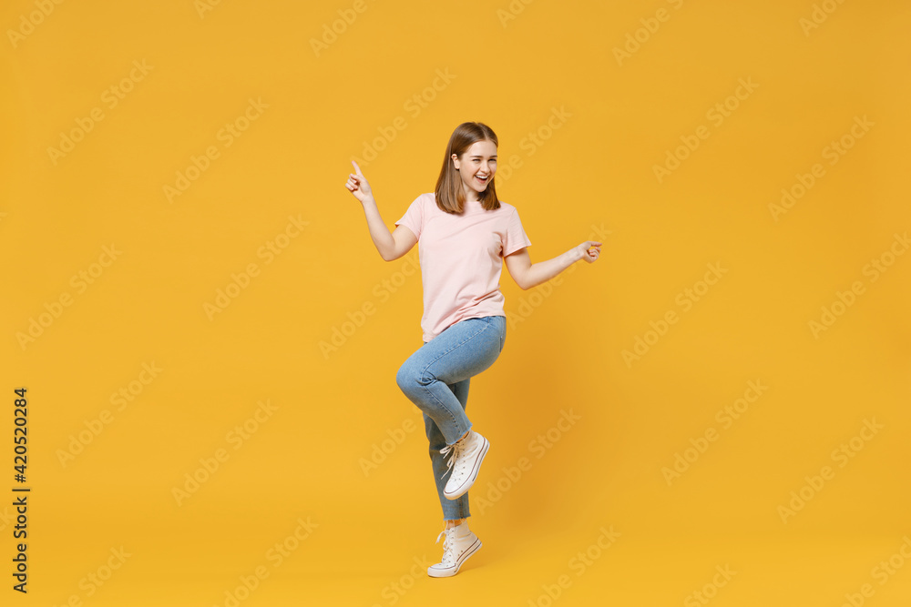 Full length of young caucasian happy satisfied excited woman 20s in casual basic pastel pink t-shirt, jeans pointing index fingers celebrating isolated on yellow color background studio portrait