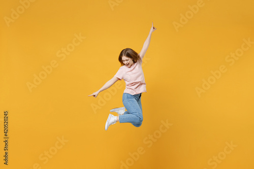 Full length of young energetic expressive caucasian hurrying up woman 20s wearing basic pastel pink t-shirt jumping high with outstretched hands isolated on yellow color background studio portrait.