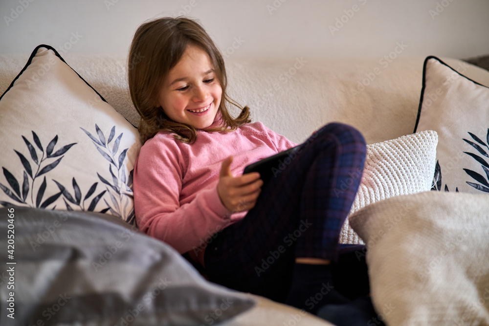 Obraz premium A little girl sitting on a couch playing with a phone 
