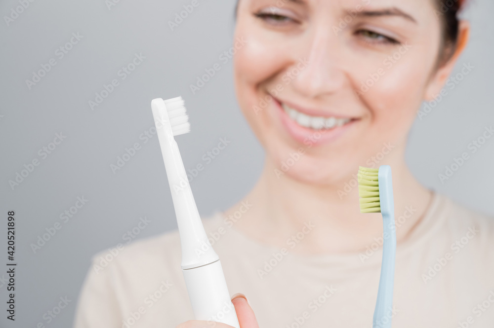 Happy woman compares a toothbrush with an electric one. The girl chooses oral hygiene products Happy woman compares a toothbrush with an electric one. The girl chooses oral hygiene products
