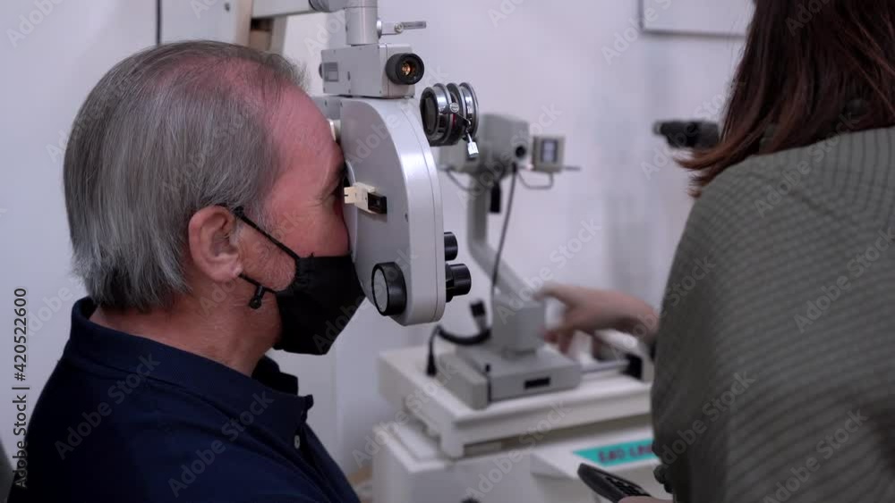 Ophthalmologist doing vision tests to an older man with white hair trying to read. hyperopia test. eyestrain test. Ophthalmologist doing vision tests to an older man with white hair trying to read. hyperopia test. eyestrain test.