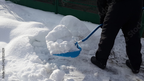 Man shoveling snow big blue shovel in the suburb. Clearing a road in winter.