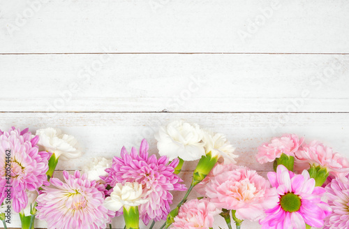 Bottom border of pink and purple flowers with mums, daisies and carnations against a white wood background. Copy space.