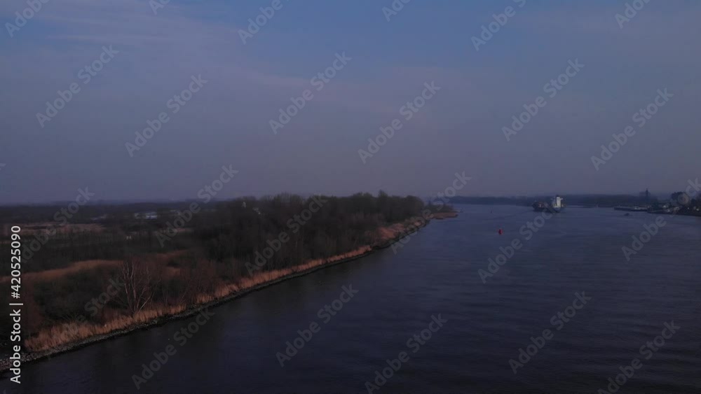 Distant View Of Industrial Ship Sailing Across Oude Maas, A River In The Town Of Puttershoek, Netherlands. wide shot Distant View Of Industrial Ship Sailing Across Oude Maas, A River In The Town Of Puttershoek, Netherlands. wide shot