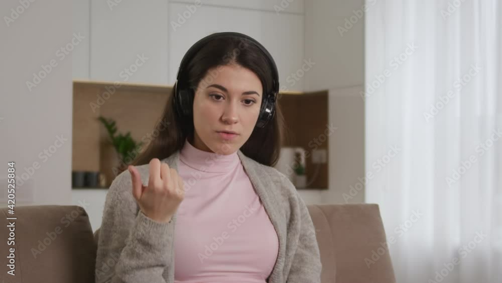 Portrait of a young 20s enterpreneur woman making a sale on a call using headphones and laptop on a couch in bright apartment Portrait of a young 20s enterpreneur woman making a sale on a call using headphones and laptop on a couch in bright apartment