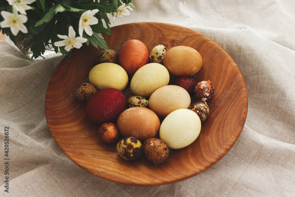 Modern easter eggs in wooden bowl on rustic linen cloth with spring flowers. Aesthetic. Happy Easter