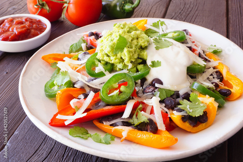 Healthy, plant based bell pepper nachos. Close up table scene on a dark wood background.