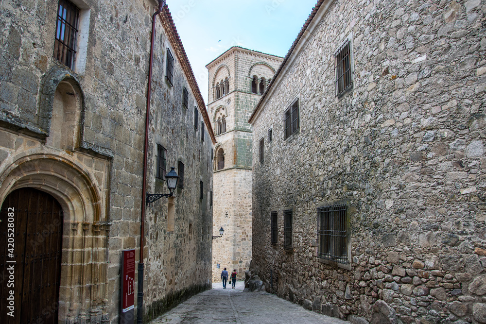 Dos casas palaciegas con fachadas de piedra convergen en una calle hacia la torre de una iglesia en la localidad española de Trujillo