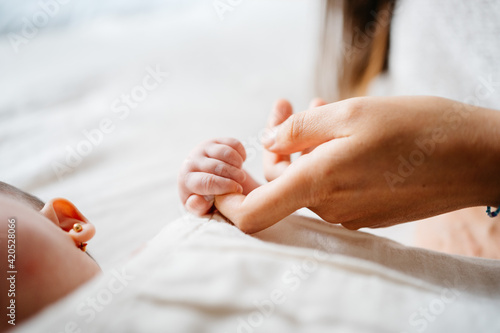 Close up of anonymous newborn baby holding unrecognizable's mother's finger on bed