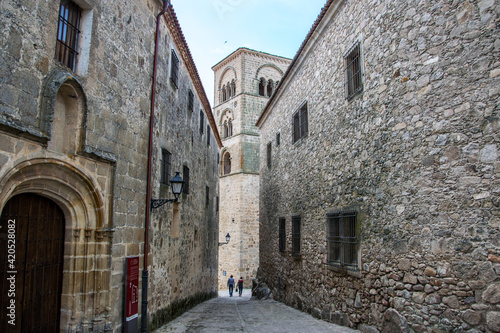 Dos casas palaciegas con fachadas de piedra convergen en una calle hacia la torre de una iglesia en la localidad espa  ola de Trujillo