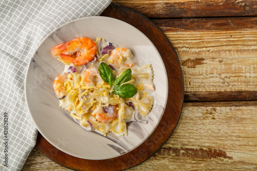 Farfalle pasta with shrimps in a creamy sauce on a gray plate on a wooden table on a light napkin.