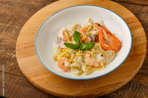 Farfalle pasta with shrimps in a creamy sauce on a gray plate on a wooden table on a round wooden stand.