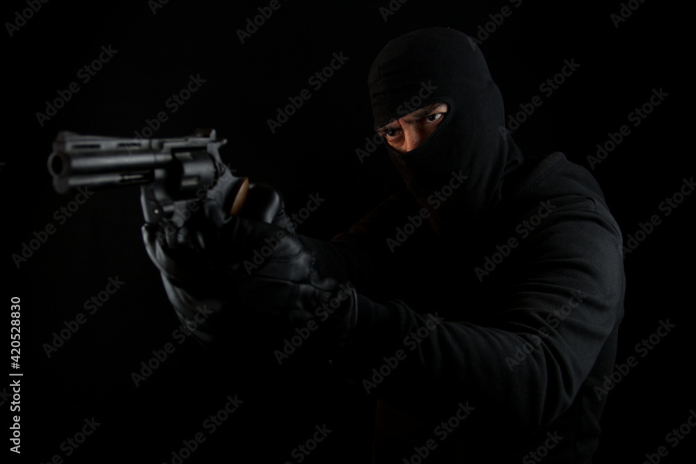 Man with black mask holding pistol, standing shooting with a gun, isolated on black background. Man with black mask holding pistol, standing shooting with a gun, isolated on black background.