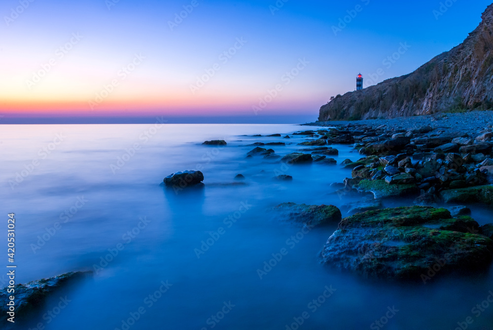 Beautiful seascape with lighthouse at sunset. Mountains and the sea with a long passage.