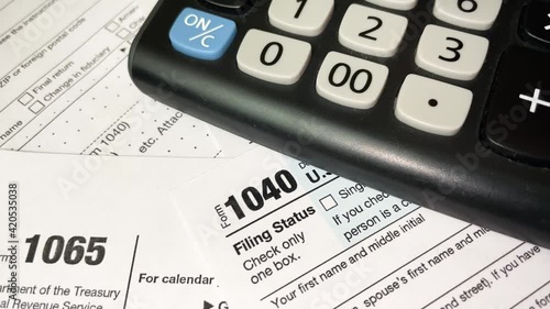 Man counting taxes on a calculator, documents on the table, tax form 1040 close up