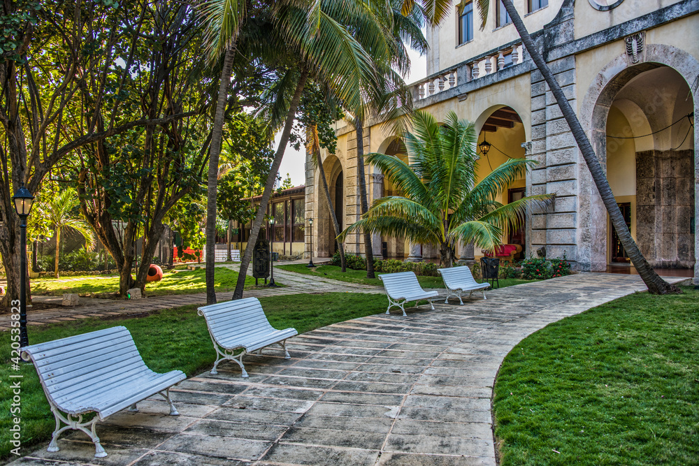 Four white benches on a path to the entrance of a building in Cuba