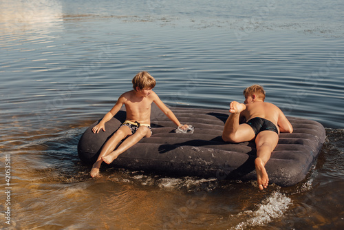 Two boys swim on an inflatable mattress