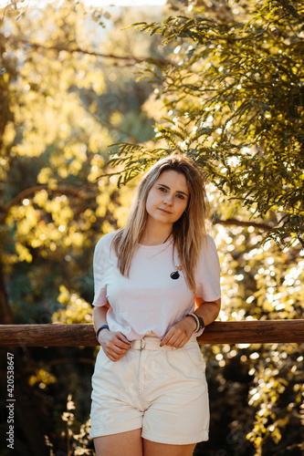 Portrait of blonde curvy girl in a green space. She is on a wooden fence. photo