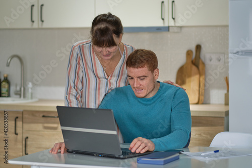 son helping aged mother paying bills online with credit card and computer. young man teaching elderly senior mother using computer applications, showing new software at home. © yavdat