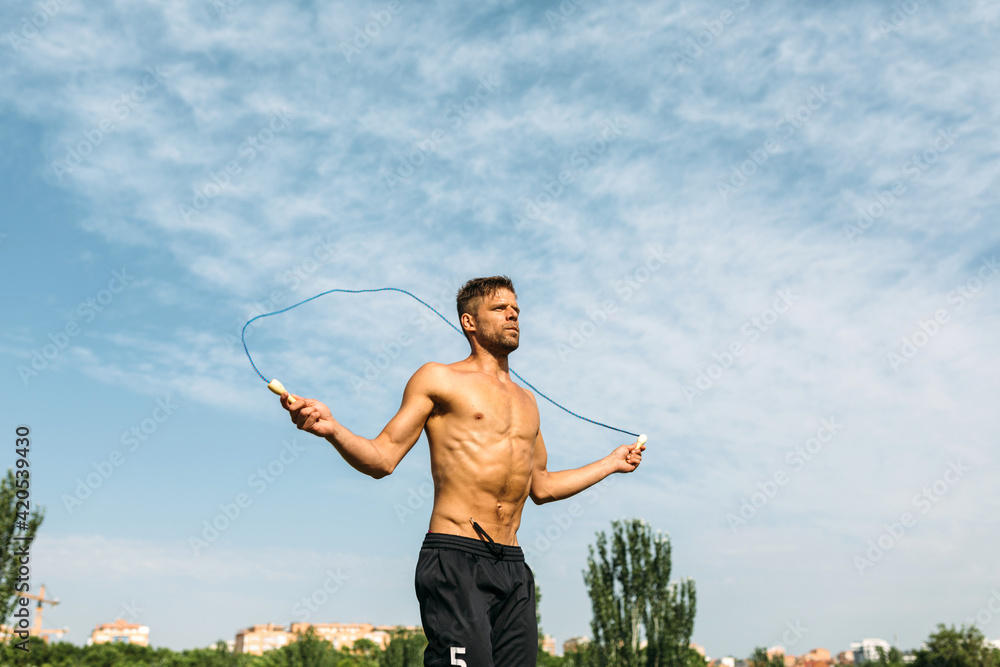 Fit sportsman jumping rope in field under cloudy sky Fit sportsman jumping rope in field under cloudy sky