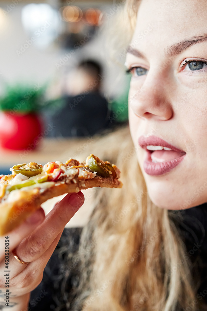 girl with blonde hair brings a slice of pizza to her mouth girl with blonde hair brings a slice of pizza to her mouth