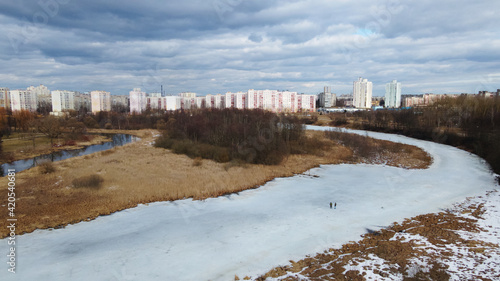 Flight over the river in the spring park. Remnants of ice are visible. In the distance, people are walking along the alleys.