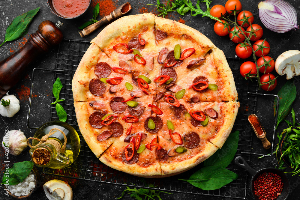 Spicy pizza with sausages and chili peppers. On a black stone background. Free space for text.