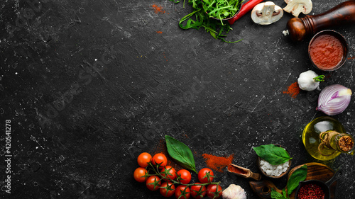Kitchen cooking background: cherry tomatoes, onions, spices and herbs. On a black background.