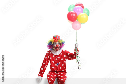 Clown sitting on a banner and holding a bunch of balloons