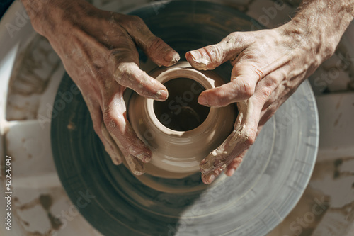 Professional potter working with clay on potter's wheel in workshop or studio