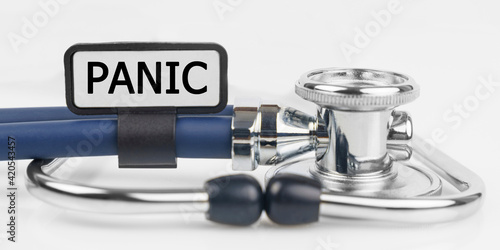 On the white surface lies a stethoscope with a plate with the inscription - PANIC